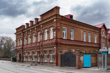 Historic brick tenement or hotel building in Ulyanovsk under an overcast sky. Architectural details and wrought iron gates highlight its historical value.