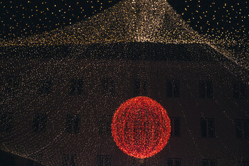 Vibrant red spherical light decoration hangs amidst a dazzling array of twinkling fairy lights,...