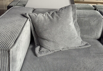 Gray corduroy pillow on matching sofa in sunlight. Cozy interior, soft fabric texture and modern...