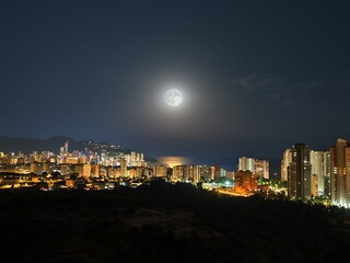 Fototapeta premium A beautifully serene night cityscape featuring a stunning full moon over the vibrant urban skyline