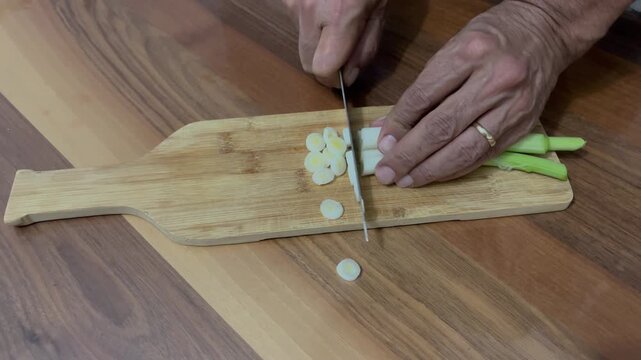 Fresh leeks are chopped on a wooden cutting board with a chef's knife. Food preparation, healthy food, top view.