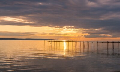 Obraz premium Sunset over calm water with a pier