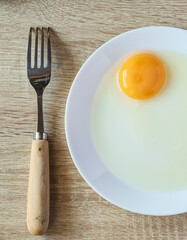 Fork and raw egg on white plate