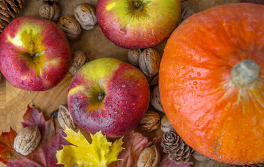 top view on bright red apples covered by drops and orange pumpkin walnuts and pine cones with autumn leaves on a table  autumnal food