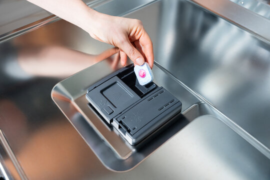 Hand inserts dishwasher detergent tablet into dispenser - tablet, detergent, dishwasher, clean, cycle.