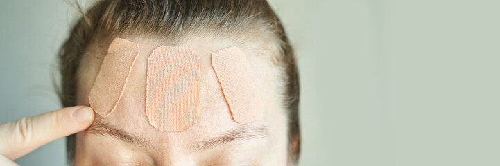 Female applying wrinkle-smoothing patches to forehead for anti-aging skincare treatment.