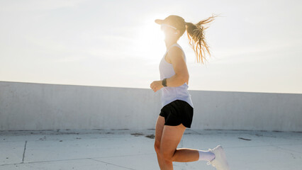Woman jogging on rooftop during early morning with sun shining behind her