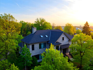 Top of a luxurious grey stucco home in Vancouver in the springtime with a shingle roof, lush trees, and lovely windows.