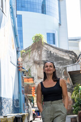 Smiling woman standing outdoors in a city with buildings in the background, concept of positive travel emotions, modern tourism and summer urban lifestyle.