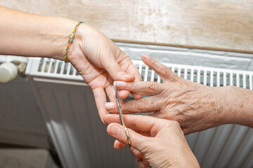 A caregiver carefully trims an elderly woman's nails with nail scissors, providing personal care and assistance