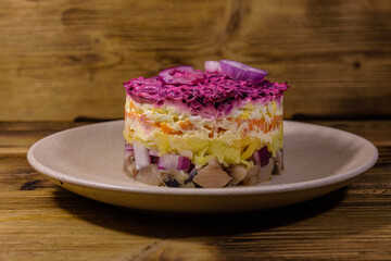 Ceramic plate with russian traditional new year salad herring under fur coat (shuba) and on rustic wooden table