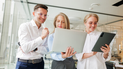 Business team collaborates on project using laptop and tablet in modern office setting