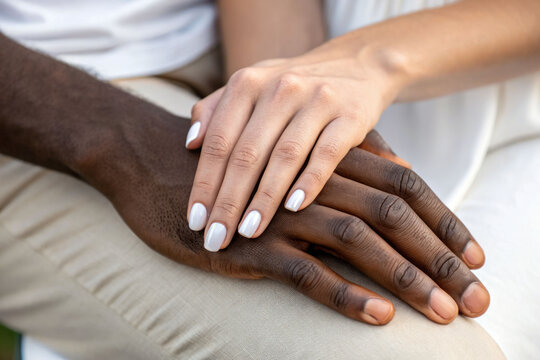 A close-up of a bride and groom's hands joined in a tender moment. Interracial couple - Powered by Adobe