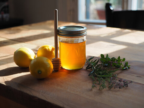 Natural ingredients for cooking or wellness: honey, fresh lemons, and aromatic herbs on a rustic wooden surface.