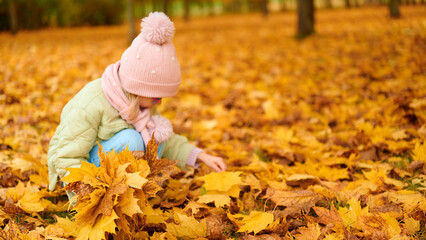 child exploring autumn leaves in park, bundled in pastel winter attire. golden foliage blankets ground, capturing essence of fall. perfect for seasonal, outdoor, family-themed content