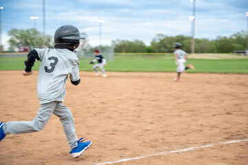 Young athlete runs towards home plate during a baseball game in a city park on a cloudy afternoon