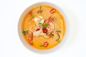 Thai tom yum soup with shrimp and mushrooms in white bowl. Garnished with red chili and green onions. Perfect for Asian menu or spicy seafood dish.