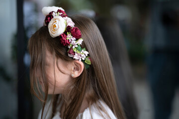 Naklejka premium Side view of a little girl in a floral wreath and white blouse standing against a glass surface, no face visible, concept of childhood and simplicity.