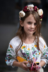 Vertical waist-up photo of a happy Ukrainian girl with loose hair in an embroidered blouse and floral wreath holding toys in her hands, concept of childhood joy and Ukrainian tradition.