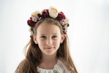 Horizontal photo of a smiling Ukrainian girl in a floral wreath and white embroidered blouse against a white background with copy space, concept of childhood and Ukrainian tradition.