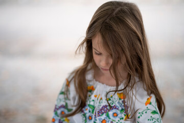 Close-up waist-up photo of a sad Ukrainian girl with loose hair in an embroidered blouse, head down, blurred background, concept of emotion and Ukrainian tradition