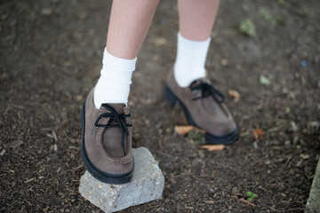 Children’s legs in white socks and leather lace-up shoes standing on stone and soil, selective focus, concept of childhood and exploration.
