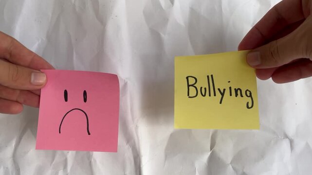 Conceptual Hand Holding Notes: Bullying Text next to red Sad Face 