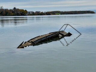 Old partially sunken wooden boat resting in calm reflective water near the shore.
