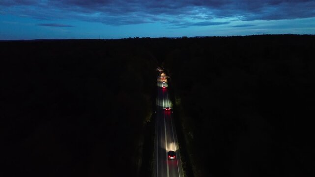 Aerial view of vehicles traveling along winding road at night, illuminated headlights cutting through darkness, showcasing dynamic motion and depth, camera follows action with smooth tracking shot