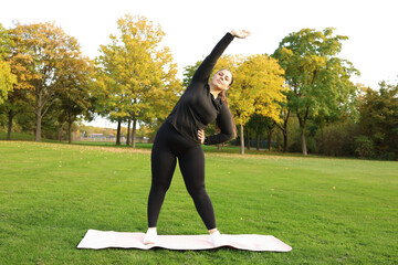 Beautiful overweight woman in sportswear doing squat exercise outdoors. Concept of body positive, self-acceptance, weight loss.
