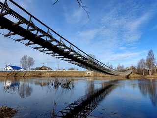Fototapeta premium A wooden suspension bridge in the village of Verkhovye, Olonetsky District, Republic of Karelia, Russia, spanning the Olonka River.