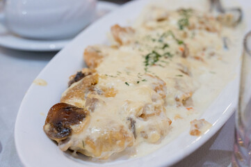 Chicken fillet with mushrooms in creamy sauce served on a white plate at a festive dining table.
