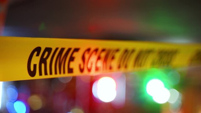 A bright yellow Crime Scene tape across an urban environment, marking a restricted area for investigation. Police or rescue team flashing lights are on the background