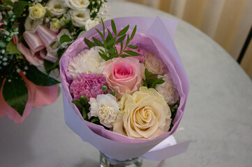 Elegant bouquet of pink, white, and cream roses and carnations wrapped in pastel paper on a table.