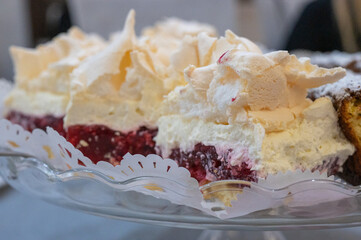 Homemade meringue cake with whipped cream and raspberry jelly layer, served on a glass plate with paper doily.