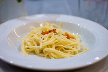 Plate of cooked spaghetti pasta with small pieces of tomato and herbs served on a white dish.