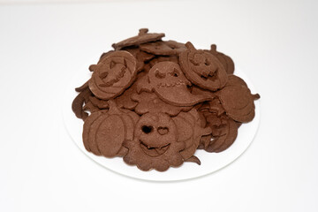 A white plate with baked cookies in the shape of pumpkins and ghosts with different emotions for a Halloween party.