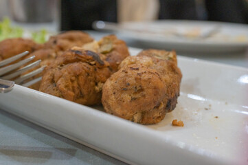 Close-up of fried meatballs served in a white ceramic dish on a dining table.