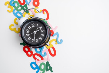 Alarm clock and scattered colorful numbers on a white desk. Concept of time management, schedule,...