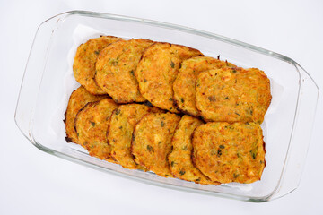 A close-up of homemade fried burgers with vegetables, neatly arranged in a heat-resistant glass dish. The golden-brown burgers look crispy on the outside with visible bits of spices and vegetables.