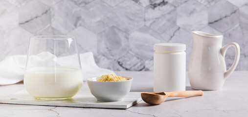 Bovine colostrum powder in a bowl, jar and diluted drink in a glass on a table web banner