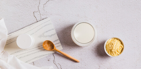 Bovine colostrum powder in a bowl and diluted drink in a glass on a table top view web banner