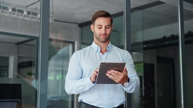 European dreaming smiling young businessman entrepreneur working on touchscreen computer device. Latin hispanic ceo business man ceo manager using tablet pad computer in office, looking at screen