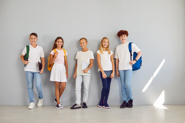 Full length portrait of happy school children looking at camera and smiling on gray wall...
