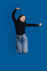 A Joyful Young Woman Jumping Against a Bright Blue Background, Exuding Energy and Happiness
