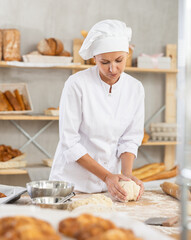 Adult female baker in uniform kneading raw dough on table