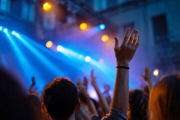 Excited crowd with hands raised under colorful stage lights at live music concert or festival party