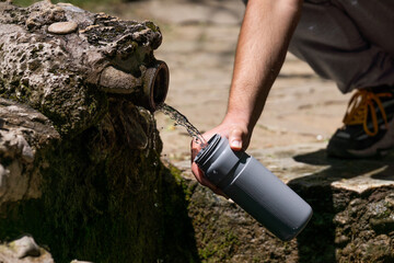 Close-up of male hand pouring drinking water from a mountain spring into a plastic bottle.
