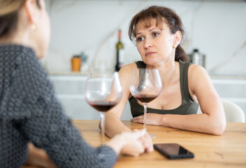 Sad woman sits silently in kitchen, female relative sympathize and comfort woman. Frustrated woman looks thoughtfully in front of her, friend ask about problems.