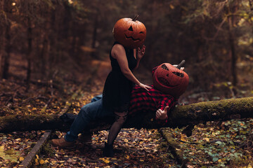 Couple in pumpkin heads celebrating autumn in a mysterious forest with vibrant fall colors
